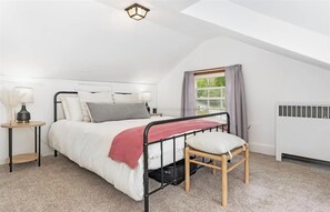 A bedroom with a bed, a nightstand, a lamp, a window with curtains, and a radiator.