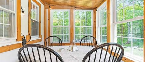 A cozy room with a wooden ceiling, large windows, and a round table with chairs.