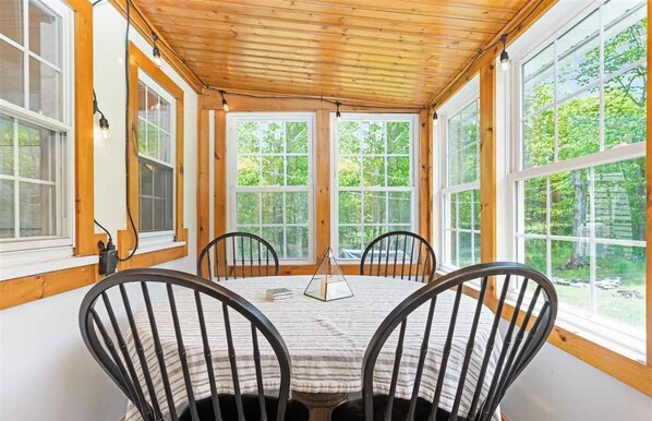 A cozy room with a wooden ceiling, large windows, and a round table with chairs.