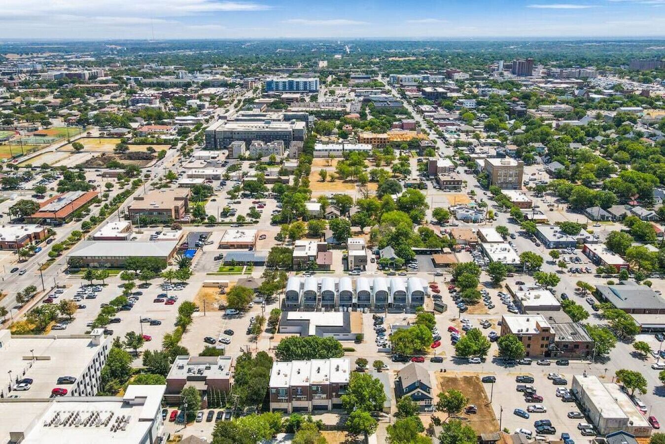 An aerial view of a cityscape with a mix of commercial and residential buildings, roads, and green spaces.