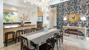 A modern kitchen with a central island, a dining area with a long table and chairs, and a decorative wall with a sun motif. - Eclectic 3-Story Townhouse - Central Location! (Fort Worth)