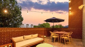 An outdoor patio with a brick wall, a wooden sofa, a round table, and chairs. - Eclectic 3-Story Townhouse - Central Location! (Fort Worth)