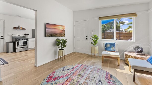 Ein modernes Wohnzimmer mit großem Fenster, einer Küche im Hintergrund und einem farbenfrohen Teppich.
