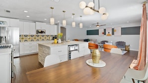 A modern kitchen with white cabinets, a wooden dining table, and pendant lighting.