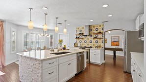 A modern kitchen with white cabinetry, a large island, stainless steel appliances, pendant lighting, and a patterned backsplash.
