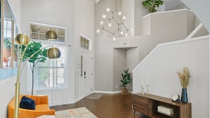 A spacious living area with a modern orange sofa, a wooden console table, and a staircase leading to an upper level.