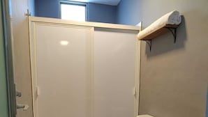 Un baño con ducha, inodoro y un estante pequeño.