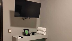 Un baño moderno con televisión montada, un perchero y una foto enmarcada sobre el lavamanos.