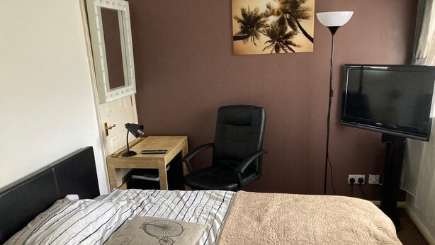 Una habitación de hotel con cama, escritorio, silla, televisor y un cuadro en la pared.