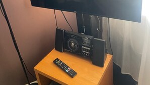 Un televisor sobre un soporte de madera, con un control remoto, un altavoz y un decodificador.