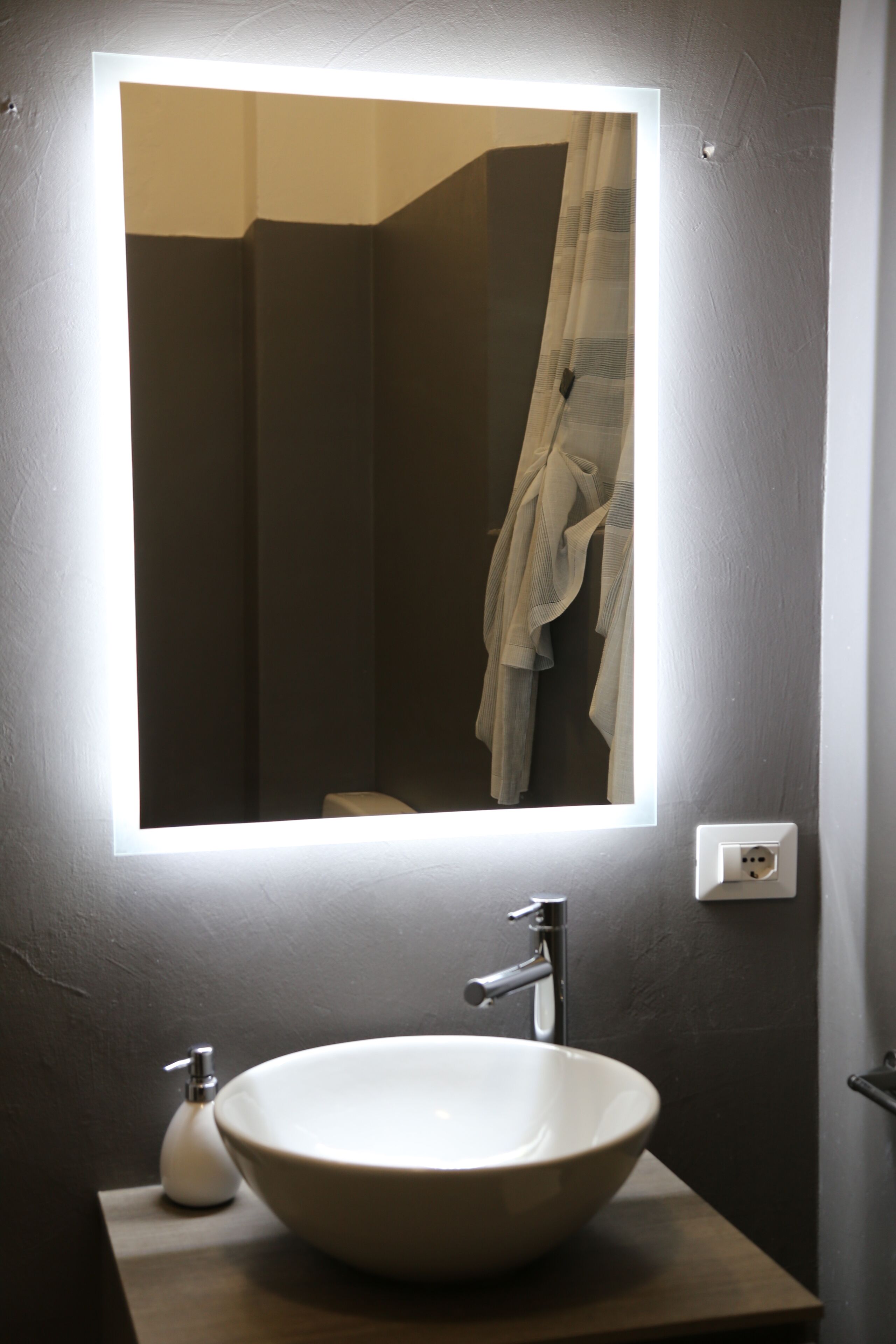 Ein Badezimmer mit einem großen Spiegel, einem weißen Waschbecken und einem Handtuch an der Wand.