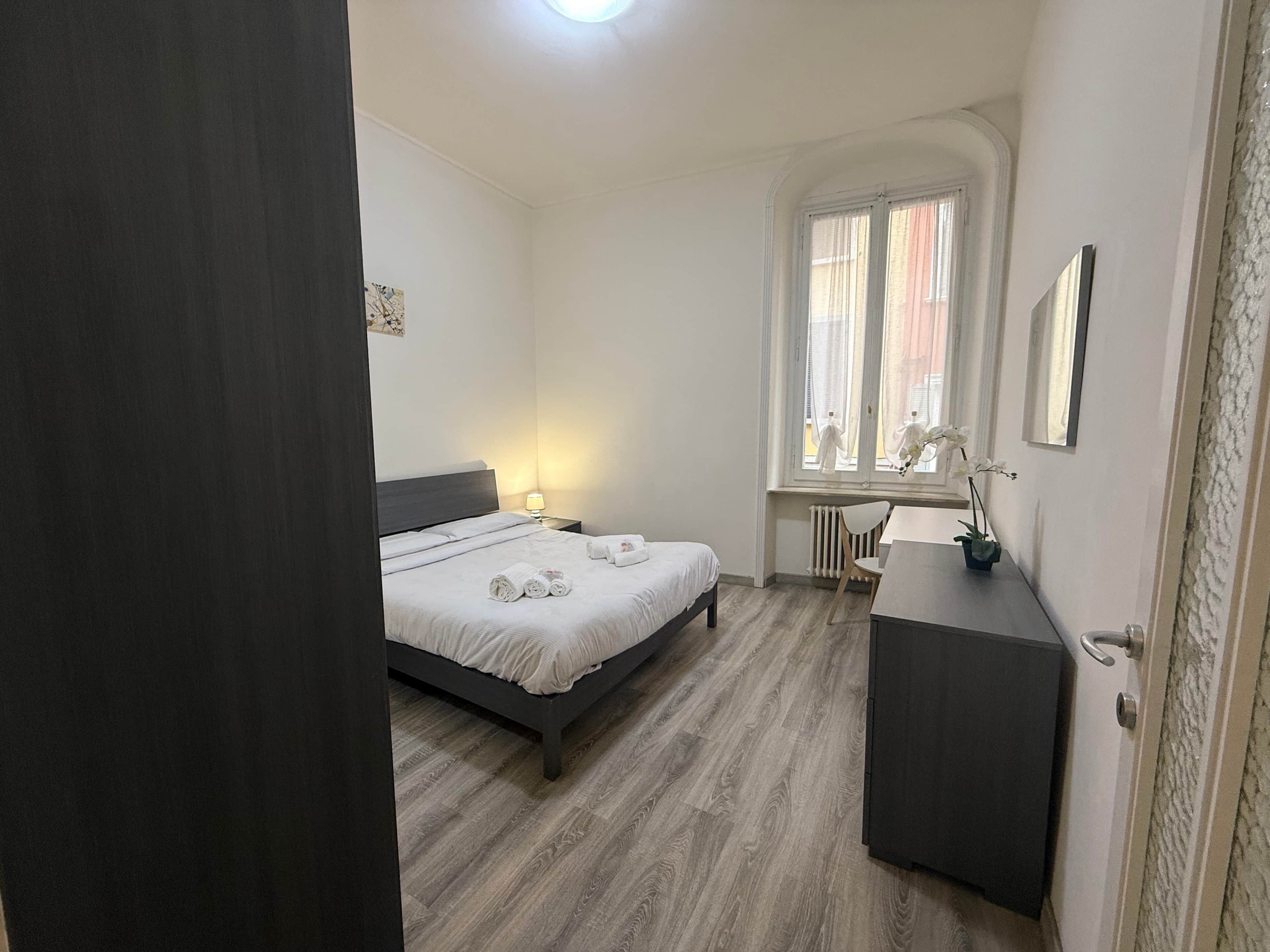 Ein Schlafzimmer mit Bett, Nachttisch, Lampe, Stuhl, Schreibtisch und Heizkörper.