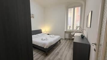 Ein Schlafzimmer mit Bett, Nachttisch, Lampe, Stuhl, Schreibtisch und Heizkörper.