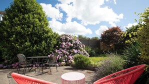 A patio area with outdoor furniture, including chairs and a table, surrounded by lush greenery and flowering plants. - Ballyroan - Peaceful, Dog Friendly Cottage (Tenby)