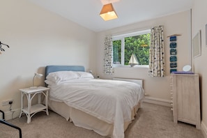 Une chambre à coucher comprenant un lit, une table de chevet, une commode, une fenêtre avec des rideaux et une vue sur la verdure à l’extérieur.