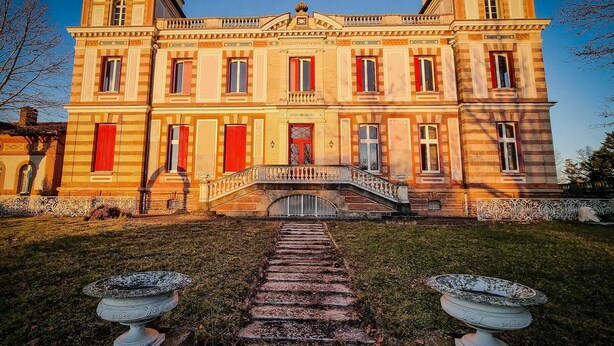 A large, historic building with a symmetrical facade, multiple windows with red shutters, and a central staircase leading to a balcony. - Charming house in a 7-hectare listed property (MONTLAUR)