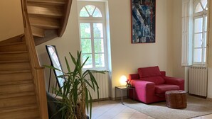 A spacious living area with a wooden staircase, a red sofa, a wicker sofa, and a large potted plant. - Charming house in a 7-hectare listed property (MONTLAUR)