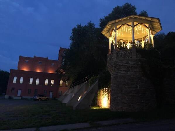 A gazebo with string lights, a stone pillar, and a building with multiple windows in the background.