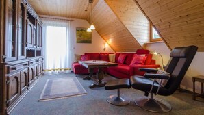 A cozy room with a red sofa, a black chair, a wooden ceiling, and a large window.