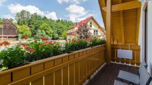 A wooden balcony with a view of a rural landscape, including houses and greenery.