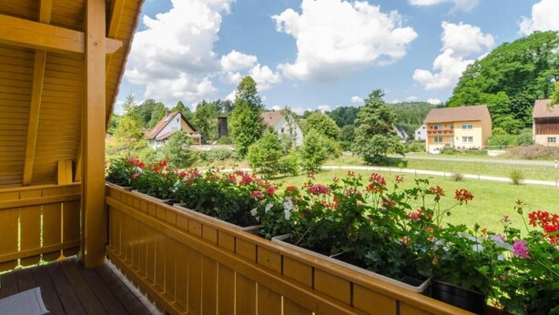 A wooden balcony with a view of houses and greenery.