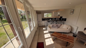 A spacious living area with a sofa, a coffee table, and a dining table. There is a kitchen area with modern appliances and a large window providing natural light. - Completely renovated cottages between Honfleur and Pont Audemer (Saint-Pierre-du-Val)