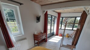 A bedroom with a bed, pillows, a wooden dresser, a TV, and a view of the outdoors. - Completely renovated cottages between Honfleur and Pont Audemer (Saint-Pierre-du-Val)
