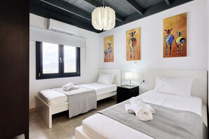 Ein Hotelzimmer mit zwei Betten, einem Fenster, Bildern an den Wänden und einer Deckenleuchte.