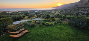 Un jardin luxuriant avec un banc en bois, un sentier et une vue sur la mer et les collines.