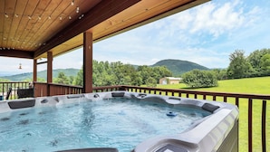 A hot tub with a wooden deck and a view of a green landscape. - This Beautiful Cabin with Mountain views is the Perfect getaway! (Townsend)