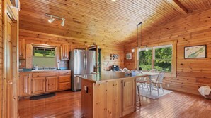 A wooden cabin kitchen with a central island, wooden cabinets, and a dining area with a view of the outdoors. - This Beautiful Cabin with Mountain views is the Perfect getaway! (Townsend)