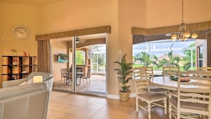 Amplia sala de estar con sofá, mesa de comedor con sillas, planta en maceta y vistas al exterior a través de grandes ventanales.