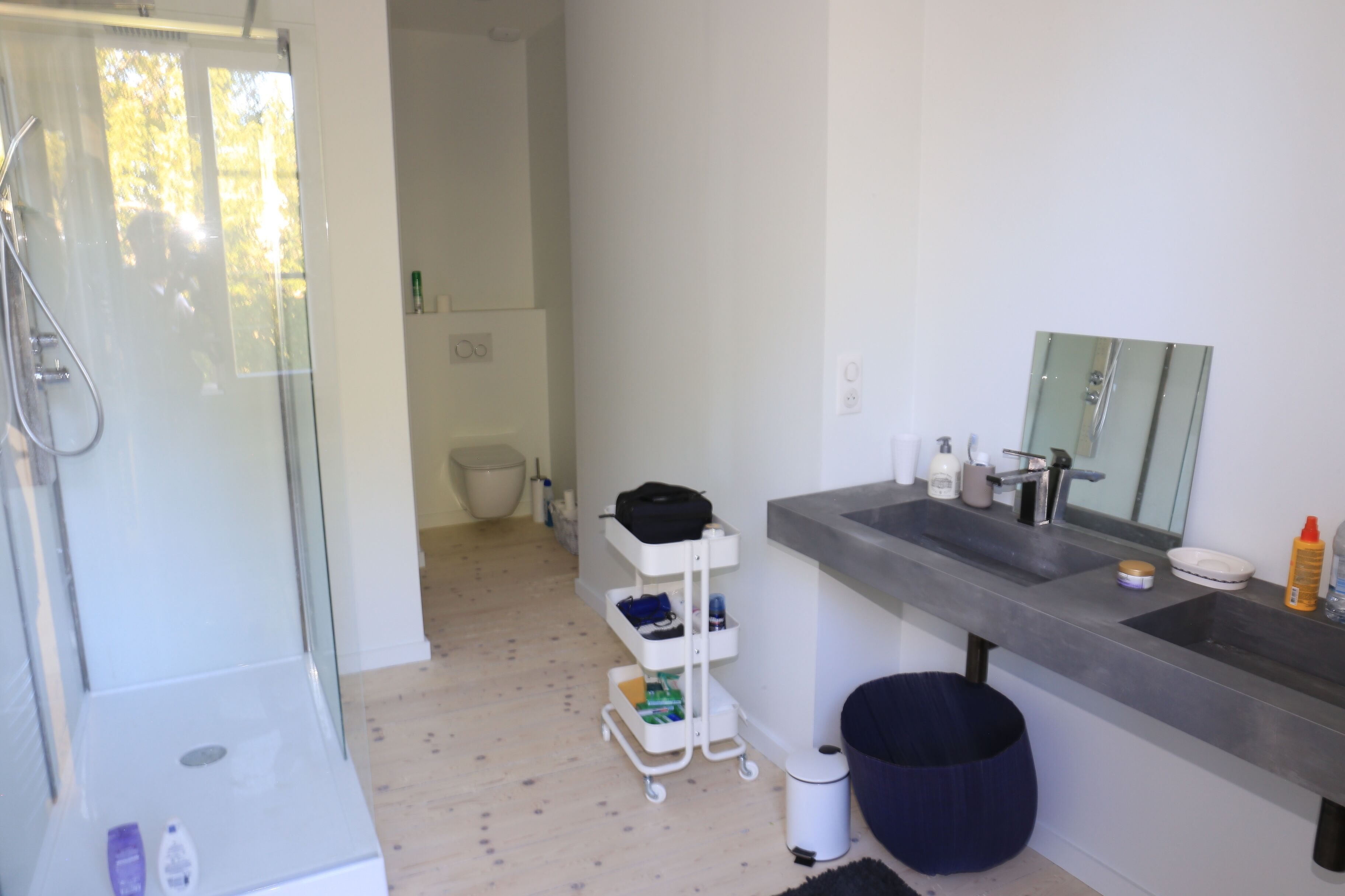 A modern bathroom with a glass shower enclosure, a white sink with a mirror, and a white storage cart.