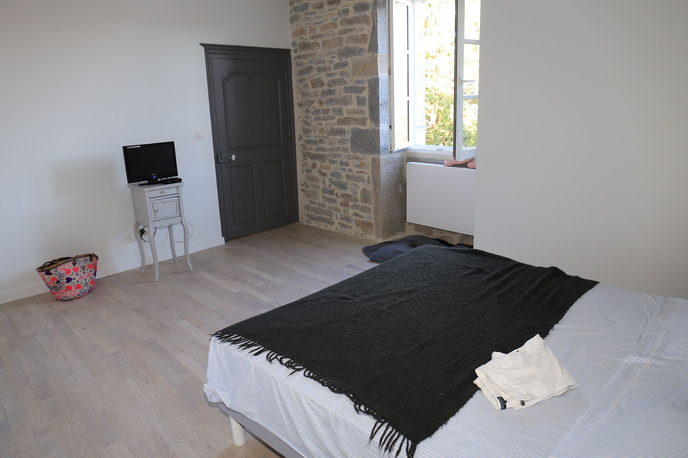 Ein Schlafzimmer mit einem Bett, einem Schreibtisch mit einem Laptop, einer Steinwand und einem Fenster.