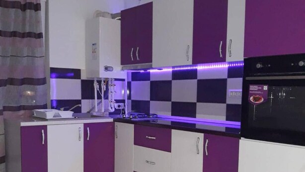 Une cuisine moderne avec des armoires violettes et blanches, un four noir et un dosseret à carreaux.
