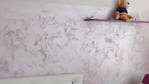 Un lit bien fait, avec une serviette pliée, une tête de lit blanche et un mur rose orné d’une étagère.
