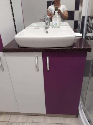 Un baño con un lavabo blanco, un mueble morado y un espejo.