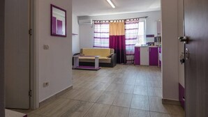 Un grand salon comprenant un canapé, une petite table et un coin cuisine avec des meubles de couleur violette.