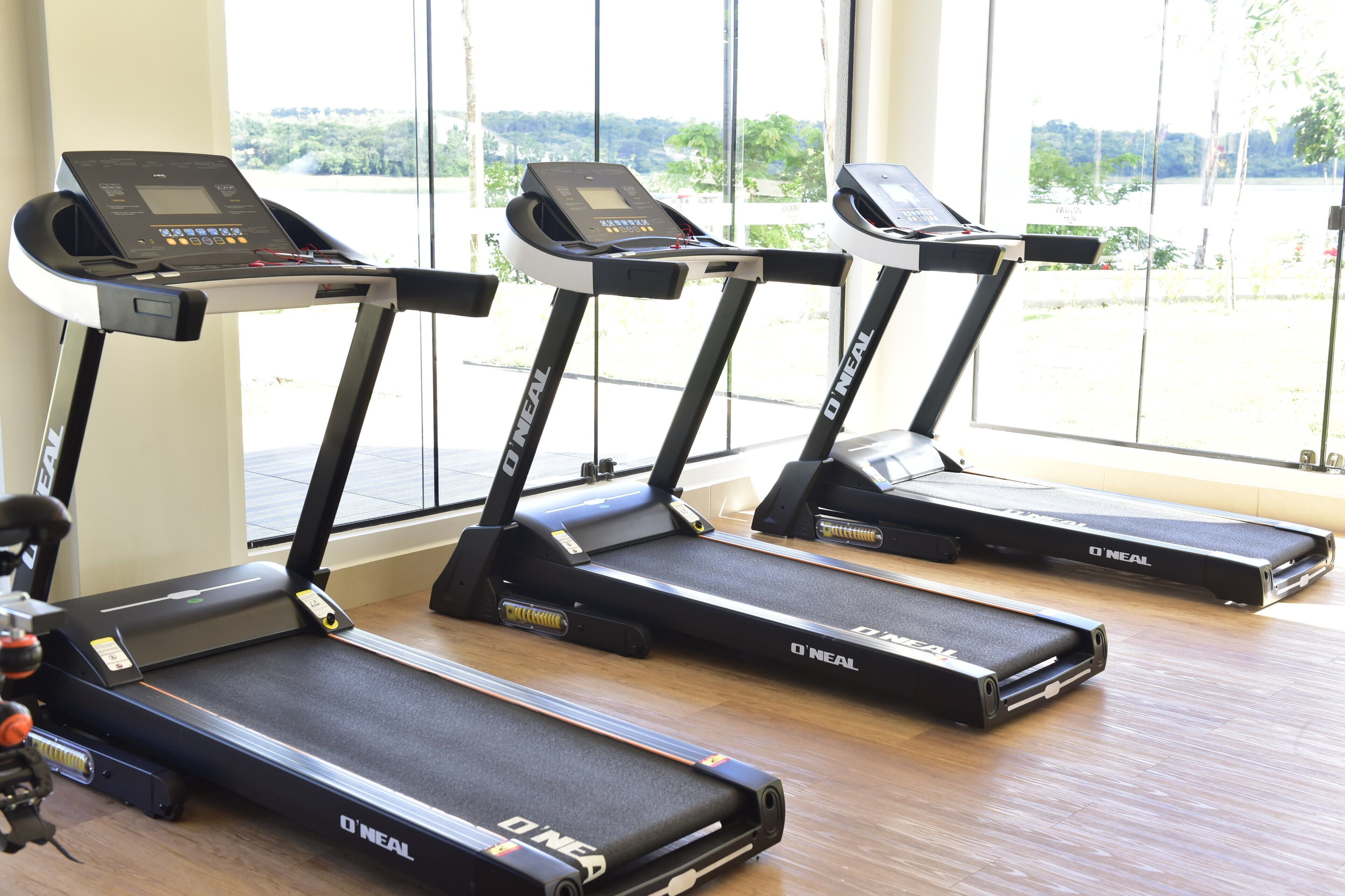Three O'Neal treadmills aligned in a row with a view of a green landscape through large windows.