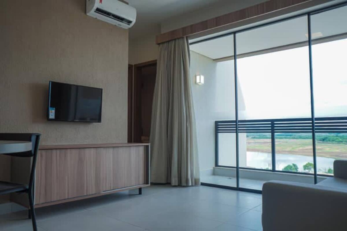 Una habitación de hotel moderna con zona de comedor, un televisor montado en la pared y un ventanal con vistas al paisaje.