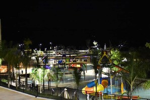 Ein Nachtblick auf einen Wasserpark mit verschiedenen Rutschen und Pools, umgeben von Palmen und beleuchtet durch künstliches Licht.