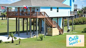 Uma casa de dois andares com varanda e deck de madeira, apoiada em estacas.