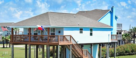 A two-story house with a wooden deck and a balcony, supported by wooden stilts.
