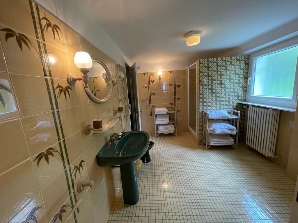 Une salle de bain avec un lavabo vert, des murs carrelés ornés de motifs en bambou, un miroir et une fenêtre donnant sur un paysage agréable.