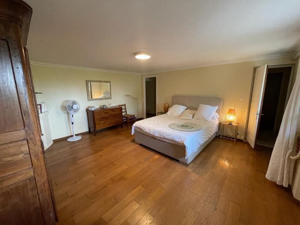 Una camera da letto con un letto grande, pavimento in legno, un comò, uno specchio e una lampada da comodino.