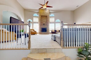 A spacious living room with a fireplace, a staircase with a railing, and a ceiling fan. - 🌄3800ft Modern Retreat ♨️Hot Tub♨️ Pool Table🧳Sleeps 18🌄Mtn Views (Albuquerque)