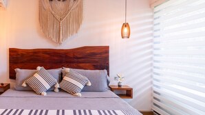 A modern bedroom with a wooden headboard, a macrame wall hanging, a hanging pendant light, and a bed with striped bedding. - TULUM XAMIRA PRIVATE SPA  BALCONY (tulum)