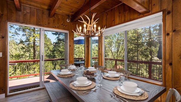 Ein Essbereich aus Holz mit einem großen Tisch, gedeckt für sechs Personen, großen Fenstern und einer Chandelier.