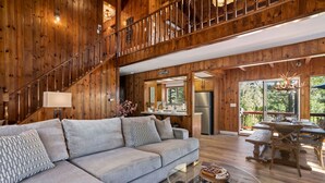 Ein geräumiges Wohnzimmer mit einer Holztreppe, einem Sofa, einem Glastisch und einem Essbereich mit Holztisch und Stühlen.