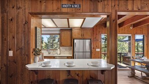 Eine Holzhüttenküche mit Kochinsel, Barhocker und Blick ins Freie.